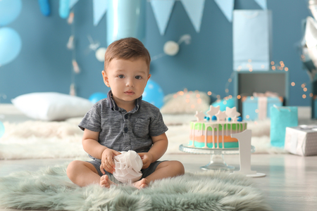 Cute little boy sitting on fluffy rug in room decorated for birthday partyの写真素材
