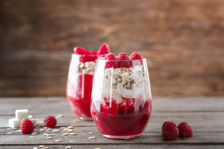 Delicious oatmeal desserts with fresh raspberries in glasses on wooden tableの写真素材