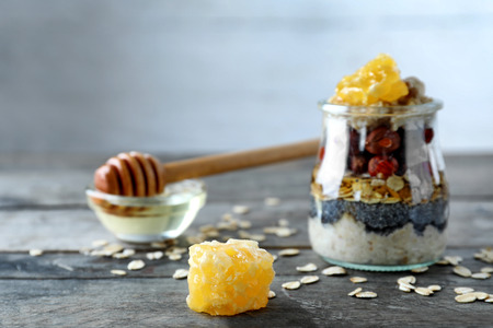 Tasty oatmeal dessert with honey and nuts in glass jar on wooden tableの写真素材