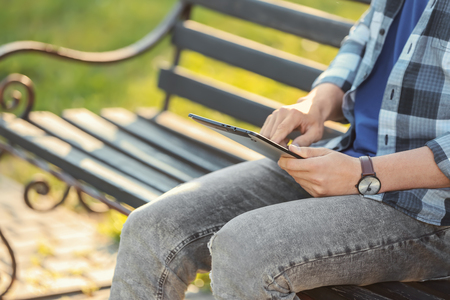 Man with tablet computer resting on bench in park, closeupの写真素材