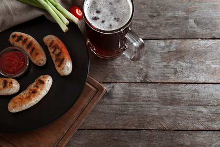 Mug of delicious beer with grilled sausages and tomato sauce on wooden tableの写真素材