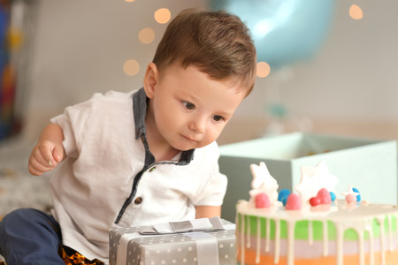 Cute little boy with gift box and birthday cake sitting on carpet in roomの写真素材