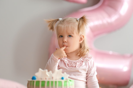 Cute little girl with delicious birthday cake sitting at homeの写真素材