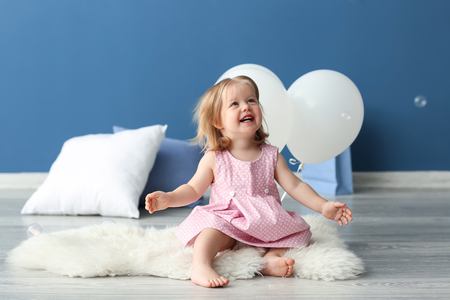 Cute little girl with air balloons sitting on rug in roomの写真素材