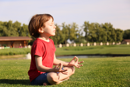 Cute little boy practicing yoga in park on sunny dayの写真素材