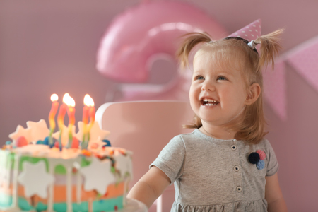 Cute little girl with birthday cake sitting on chair in roomの写真素材