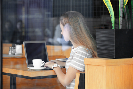 Young female freelancer with laptop working in cafe, view through glass windowの写真素材