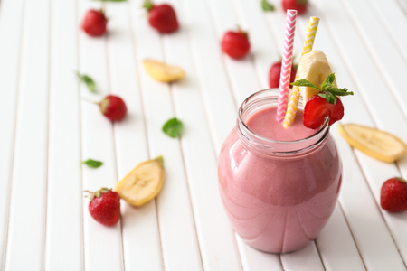 Glass jar with tasty strawberry smoothie on wooden tableの写真素材