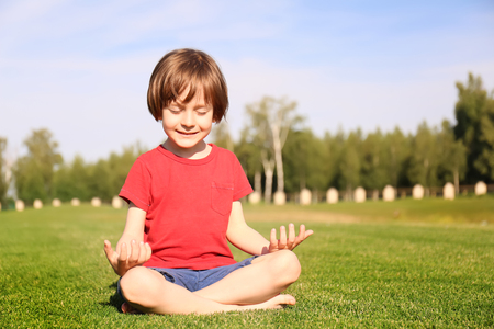 Cute little boy practicing yoga in park on sunny dayの写真素材