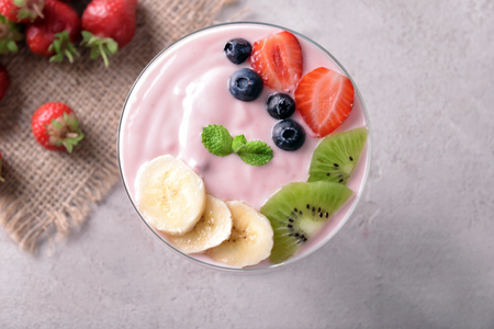 Glass bowl with strawberry yogurt and fresh fruits on grey backgroundの写真素材