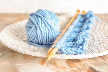 Ball of knitting yarn with needles on plate, closeup