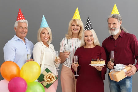 Mature people celebrating birthday with tasty cake and champagne on grey background