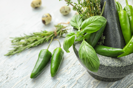 Mortar with fresh chili peppers and herbs on light backgroundの写真素材