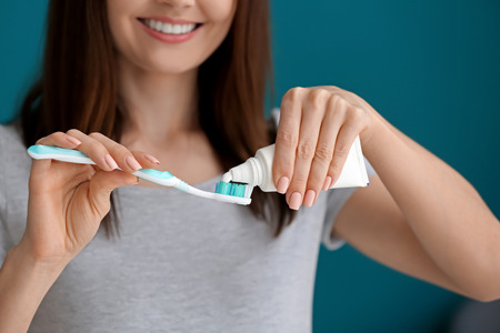 Young woman squeezing toothpaste on brush against color backgroundの写真素材