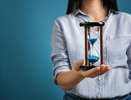 Woman holding hourglass on color background, closeup. Time management conceptの写真素材