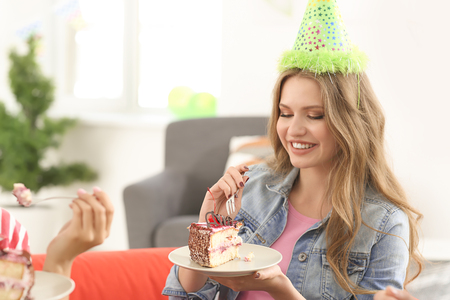 Young woman eating tasty cake at birthday party indoorsの写真素材