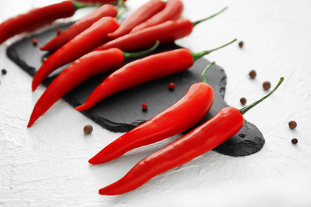 Slate plate with fresh chili peppers on light background