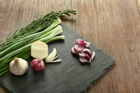 Slate plate with fresh onions, garlic and herbs on wooden tableの写真素材