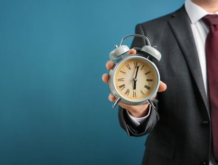 Businessman holding alarm clock on color background. Time management concept