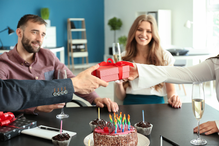 Young man giving birthday present to his colleague at party in officeの写真素材