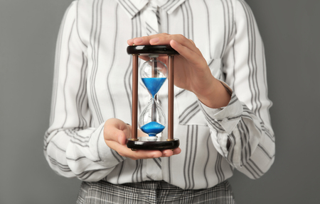 Woman holding hourglass on grey background. Time management conceptの写真素材