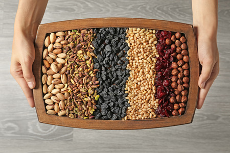 Woman holding wooden tray with different nuts and dried fruits on light background