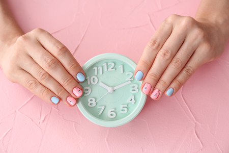 Woman with stylish color nails holding alarm clock on pink background, closeupの写真素材