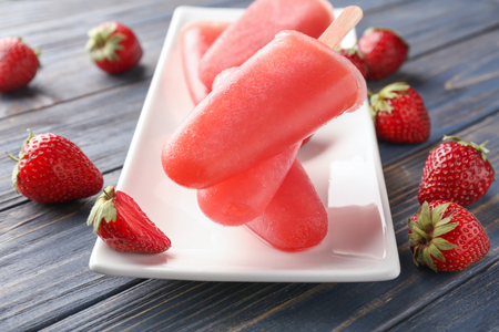 Plate with delicious strawberry popsicles on wooden tableの写真素材