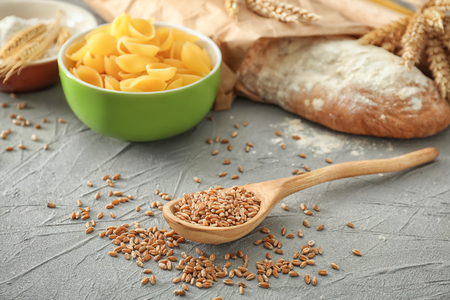 Spoon with wheat grains and products on tableの写真素材