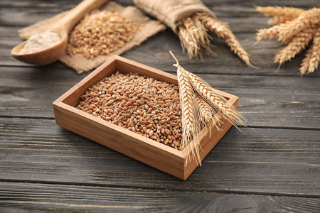 Wooden box with wheat grains and spikelets on tableの写真素材