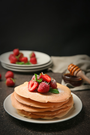 Plate with delicious pancakes and strawberries on table against dark backgroundの写真素材
