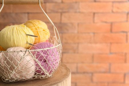 Basket with knitting yarn on wooden table near brick wallの写真素材