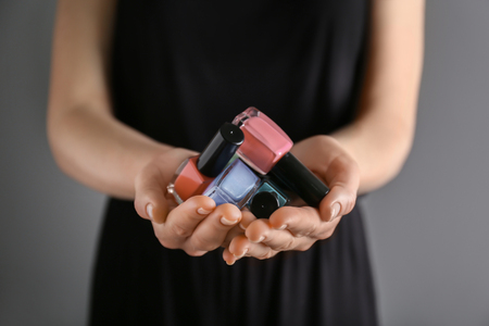 Woman holding bottles of nail polishes on grey background, closeupの写真素材