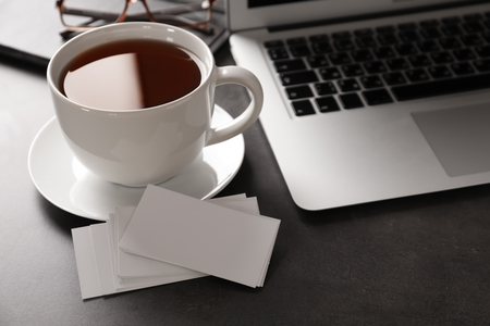 Blank business cards with laptop and cup of tea on grey tableの写真素材