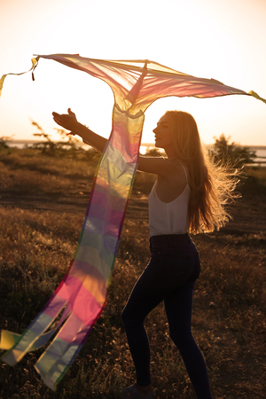 Beautiful young woman flying kite outdoors at sunsetの写真素材