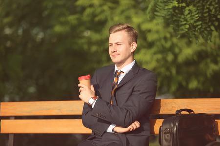 Young man in formal clothes resting with cup of coffee in park on sunny dayの写真素材