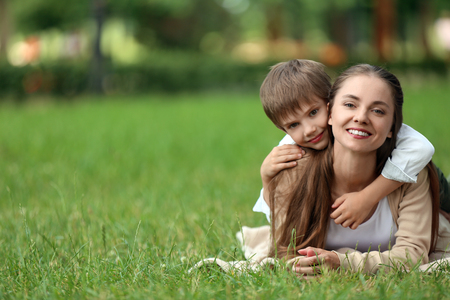 Happy mother and son resting on plaid in green parkの写真素材