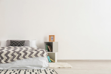 Big comfortable bed with shelf unit near light wallの写真素材