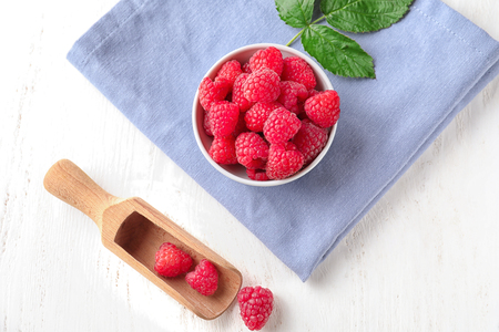 Bowl and scoop with ripe aromatic raspberries on white wooden table