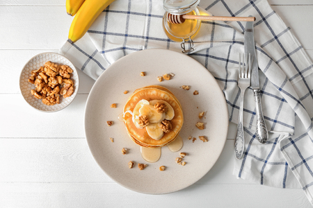 Plate with tasty pancakes, walnuts and sliced banana on tableの写真素材