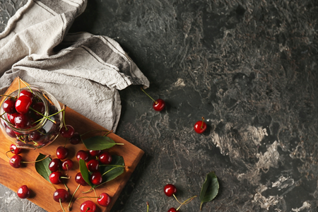 Glass jar and wooden board with fresh ripe cherries on grey textured backgroundの写真素材