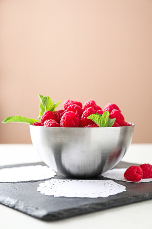 Bowl with delicious raspberries on slate plate against color backgroundの写真素材