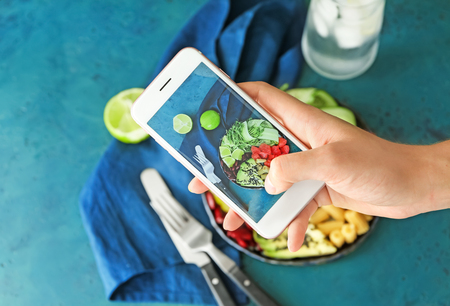 Woman taking photo of delicious fresh salad with mobile phoneの写真素材