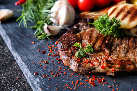 Tasty grilled meat with vegetables and herbs on slate plateの写真素材
