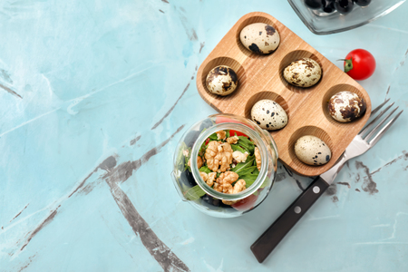 Delicious vegetable salad in jar and holder with quail eggs on tableの写真素材
