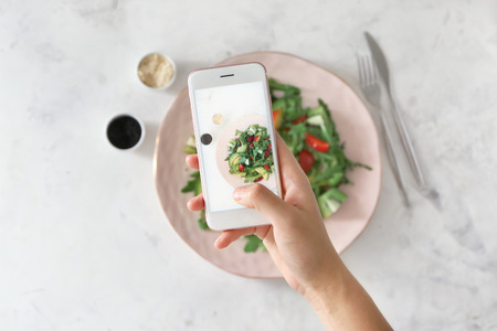 Woman taking photo of healthy fresh salad with mobile phoneの写真素材