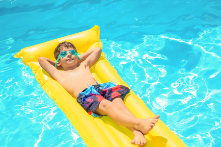 Cute little boy relaxing on inflatable mattress in swimming poolの写真素材