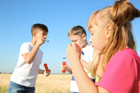 Cute little children blowing soap bubbles in field on sunny dayの写真素材
