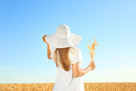 Beautiful woman with wheat spikelets in field on sunny dayの写真素材
