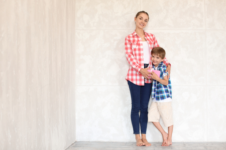 Happy mother with son holding gift box near light wall indoors. Mother's day celebrationの写真素材